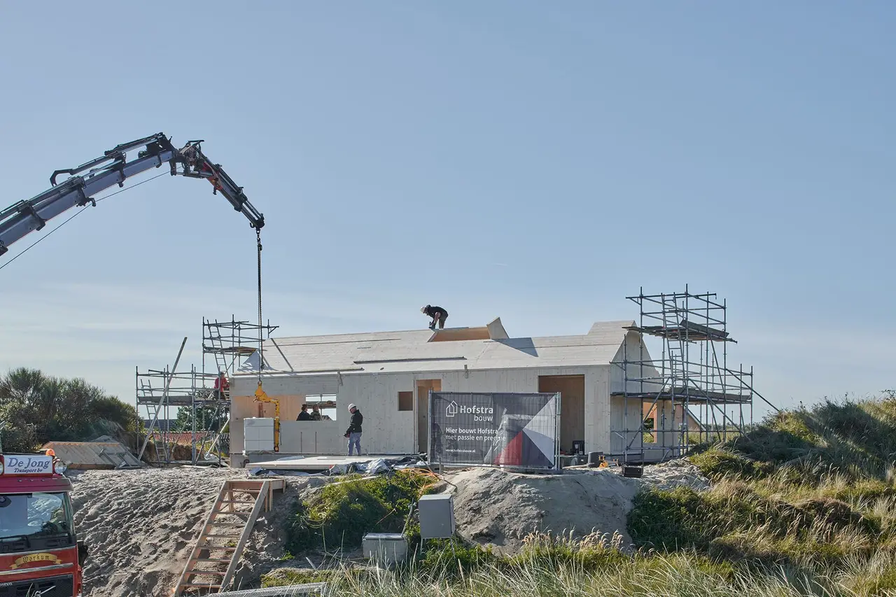 Kraan en steigers rond de woning, met de baksteen op de voorgrond.