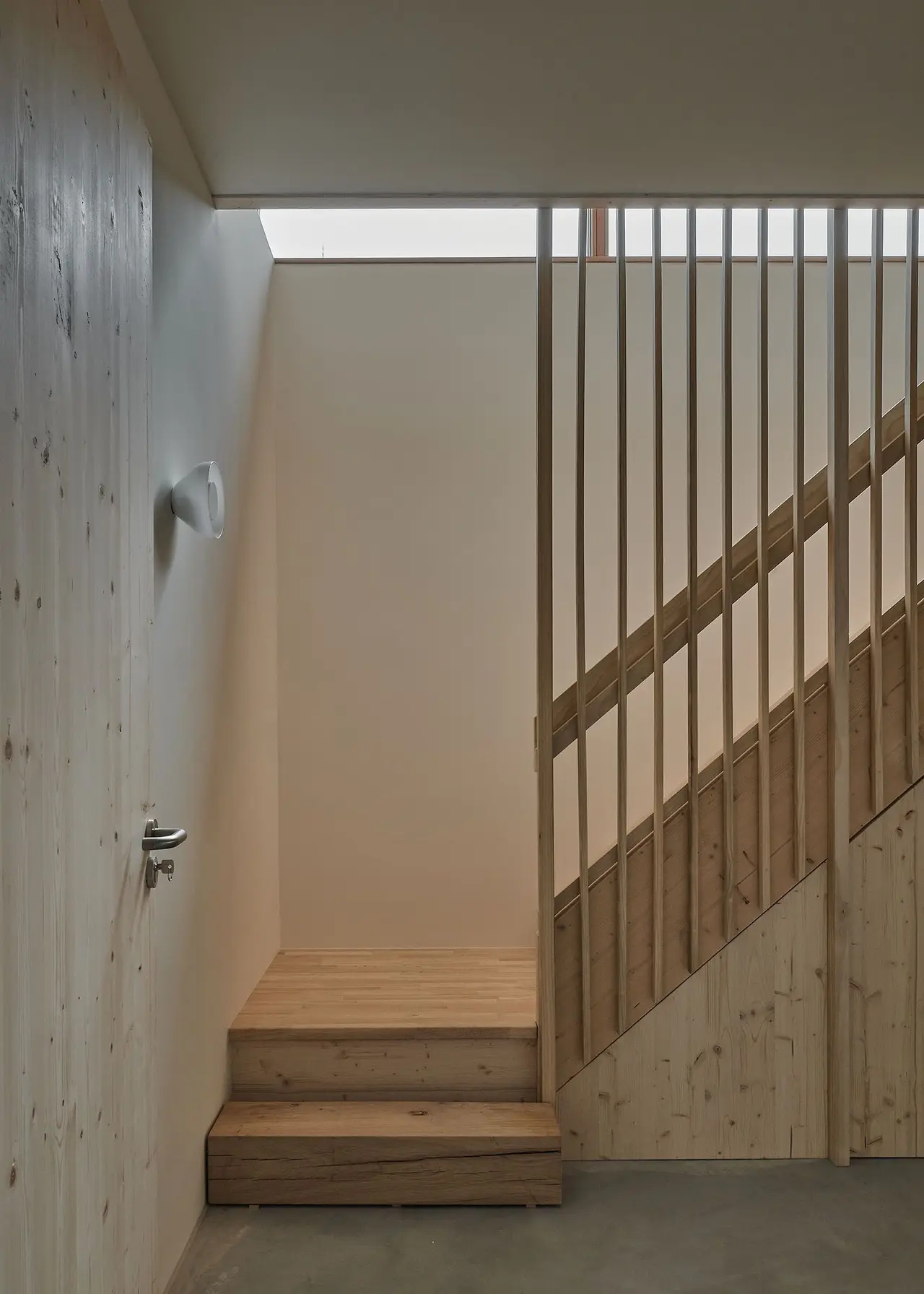 De houten trap met lamellen naar het souterrain, verlicht door een daklicht.